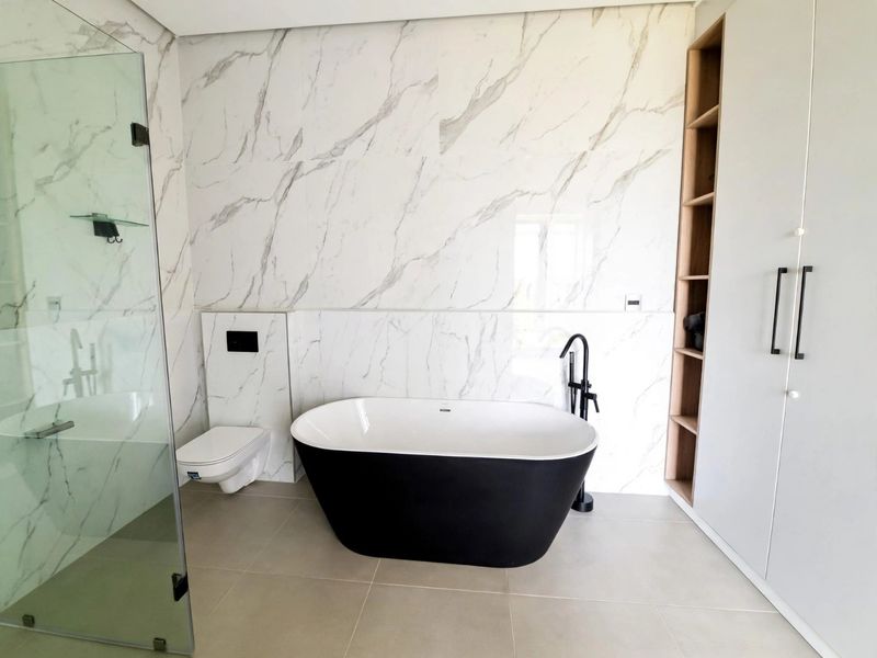 Modern bathroom featuring a freestanding black bathtub, wall-mounted toilet, glass shower enclosure, and elegant marble-look wall tiling with matte black fixtures.