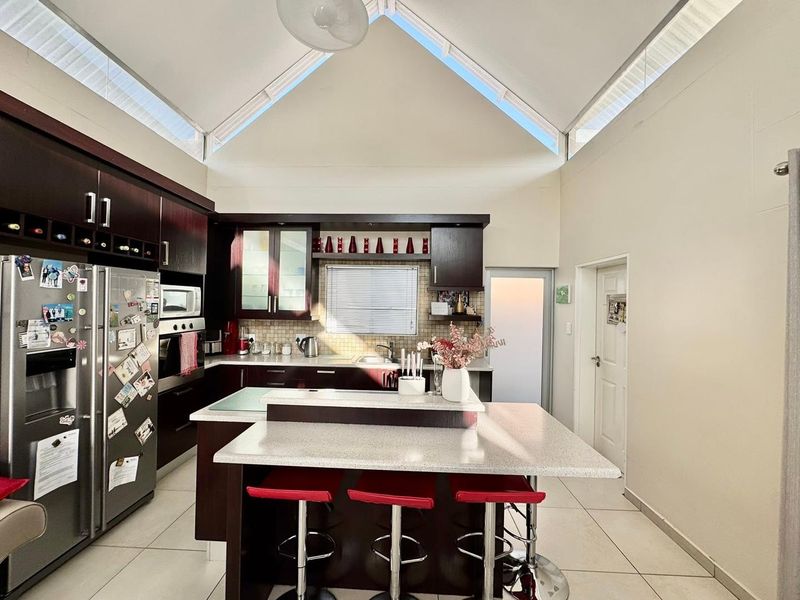 Modern kitchen featuring dark wood cabinetry, stone countertops, a central island, and a striking vaulted ceiling with clerestory windows for natural light.