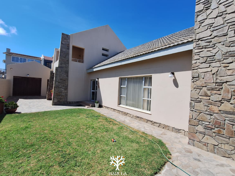 Rear view of the property featuring stone cladding accents, a tiled roof, paved driveway, and a well-maintained lawn area.