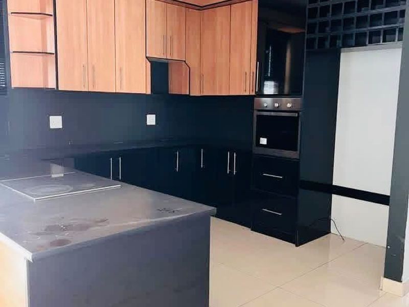 Modern kitchen featuring two-tone cabinetry, built-in oven, hob, integrated wine rack, and stone countertops with tiled flooring.
