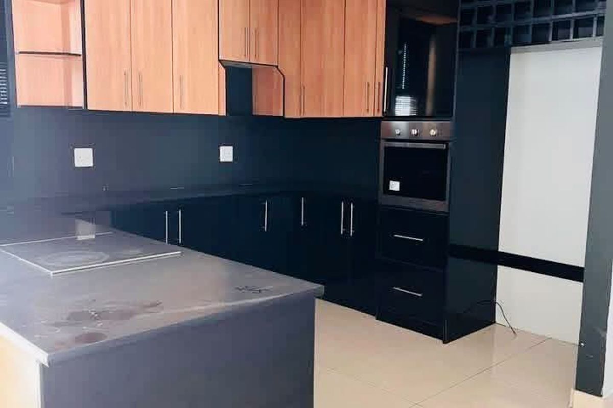 Modern kitchen featuring two-tone cabinetry, built-in oven, hob, integrated wine rack, and stone countertops with tiled flooring.