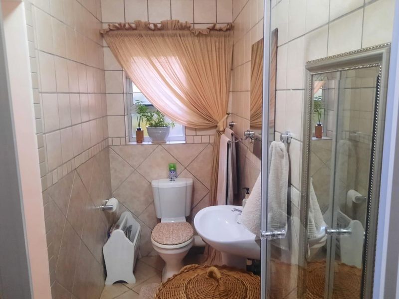A compact bathroom featuring a pedestal basin, toilet, and shower enclosure with neutral ceramic wall and floor tiling.