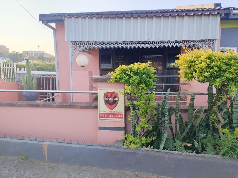 Front facade of the house featuring a covered porch area, stainless steel railings, and a perimeter wall with security fencing.