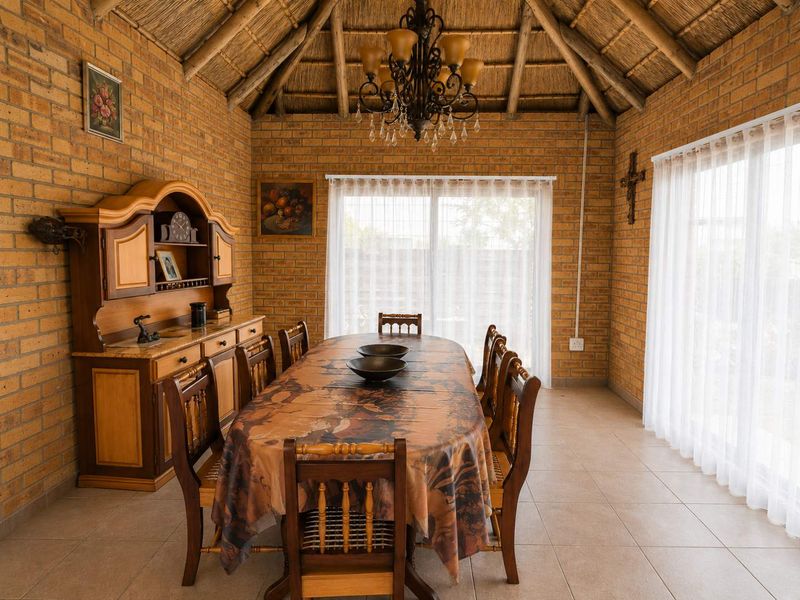 Spacious dining room featuring exposed brick walls, a high thatched ceiling with timber rafters, tiled floors, and large sliding doors providing natural light.