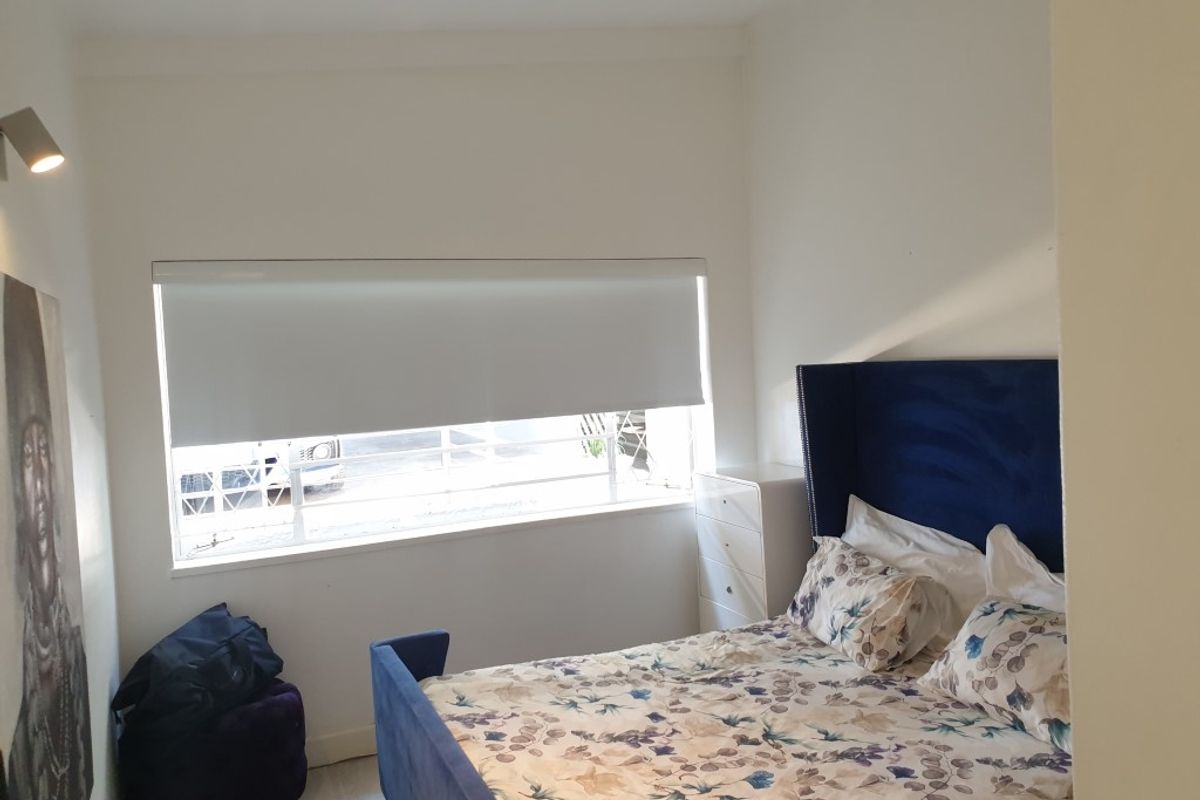 A well-lit bedroom featuring a large window with a roller blind, neutral walls, and modern downlighting.