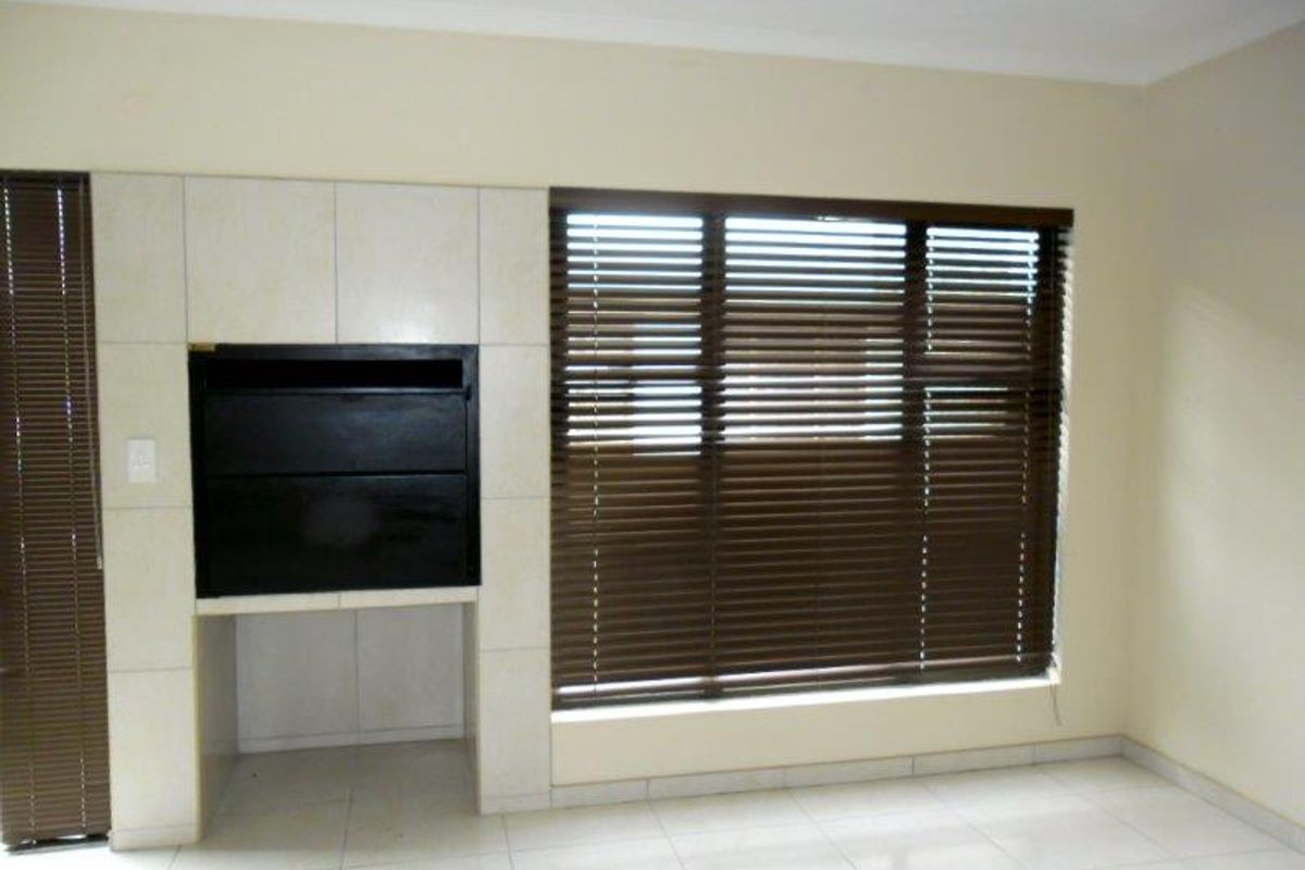 Spacious living area featuring a built-in fireplace, neutral tiled flooring, and large windows fitted with venetian blinds.
