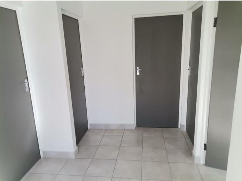 A clean and neutral hallway featuring light-colored floor tiles and multiple internal doors with dark finishes.