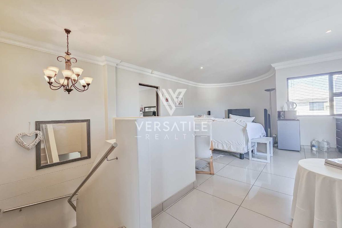 Spacious bedroom area featuring tiled flooring, recessed lighting, and a decorative chandelier, with an open-plan layout leading to the staircase.