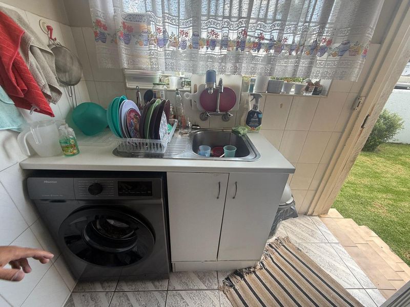 A functional laundry area featuring a stainless steel sink, tiled splashback, and built-in cabinetry with direct access to the garden.