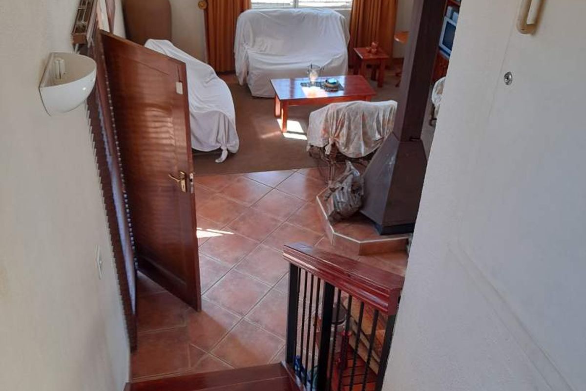 View from a wooden staircase looking down into a living area featuring terracotta floor tiles and a built-in fireplace.