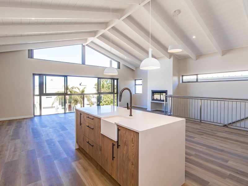Spacious open-plan living area featuring a modern kitchen island with farmhouse sink, vaulted ceilings with exposed beams, and a built-in fireplace.