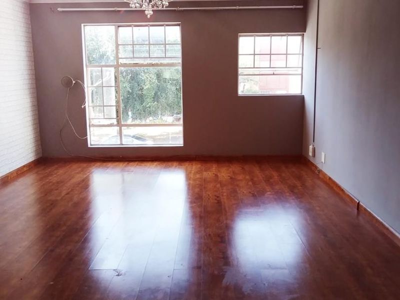 An empty living room featuring polished laminate flooring, an exposed brick feature wall, and classic ceiling cornicing with natural light from multi-pane windows.