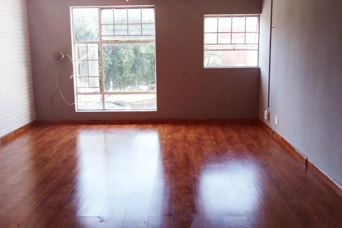 An empty living room featuring polished laminate flooring, an exposed brick feature wall, and classic ceiling cornicing with natural light from multi-pane windows.