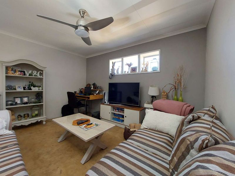 A comfortable living room featuring a ceiling fan, coved ceilings, and high-level windows that provide natural light.