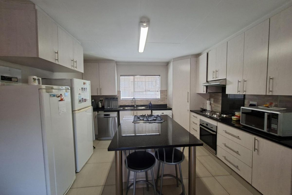 A functional kitchen featuring light-toned cabinetry, dark granite countertops, a central island with a built-in gas hob, and tiled flooring.