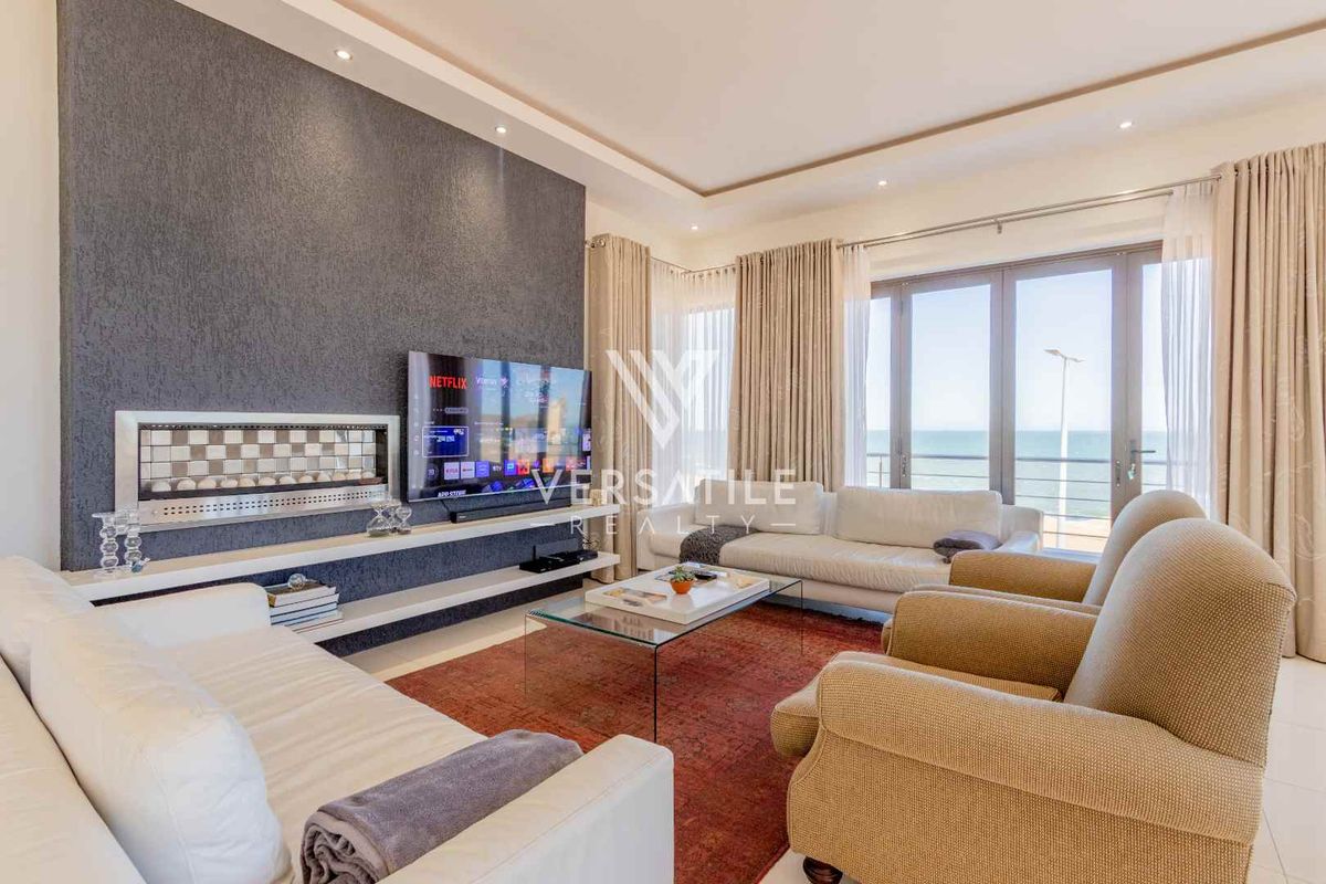 Spacious living room featuring a textured feature wall, built-in fireplace, recessed ceiling lighting, and large glass doors opening to a scenic ocean view.