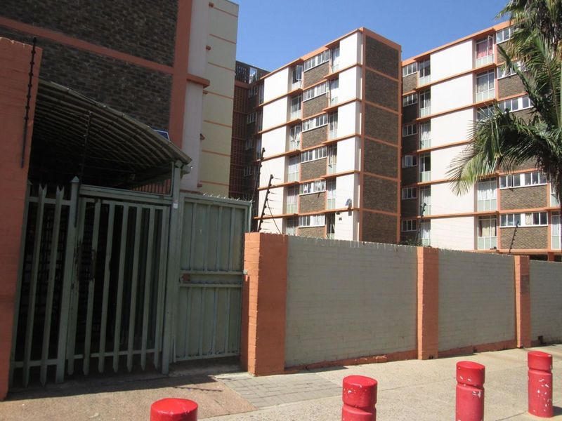Exterior view of an apartment complex featuring a secure gated entrance, perimeter wall with electric fencing, and multi-story residential blocks.