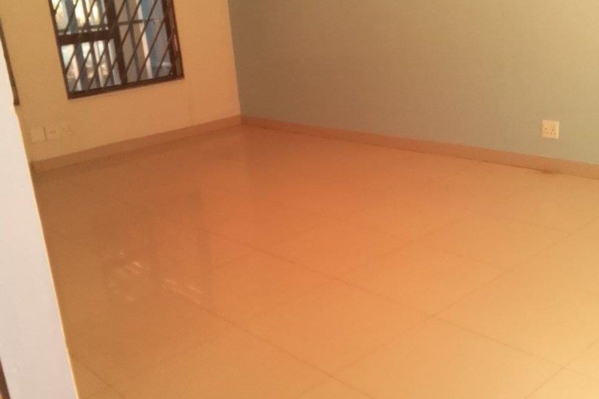 An empty, neutrally painted living area featuring tiled flooring and a window with security bars.