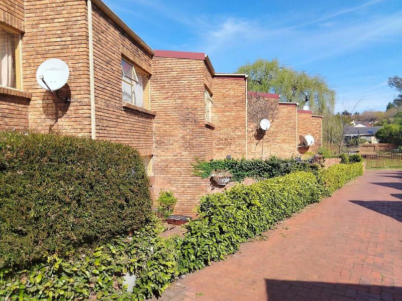 A view of the townhouse complex exterior featuring face brick facades, paved walkways, and established garden hedges along the front elevation.