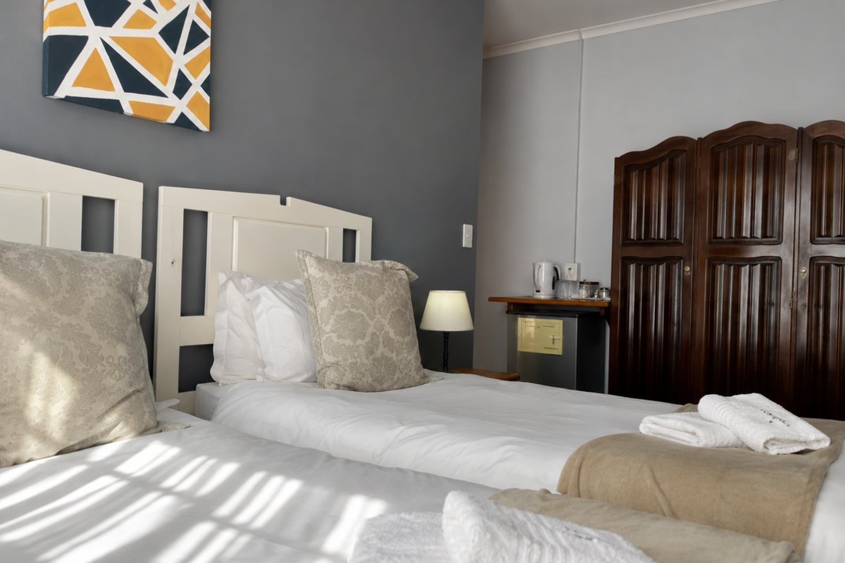 A bedroom featuring twin beds with white headboards, a dark wood wardrobe, and a small built-in refreshment area with a mini-fridge.