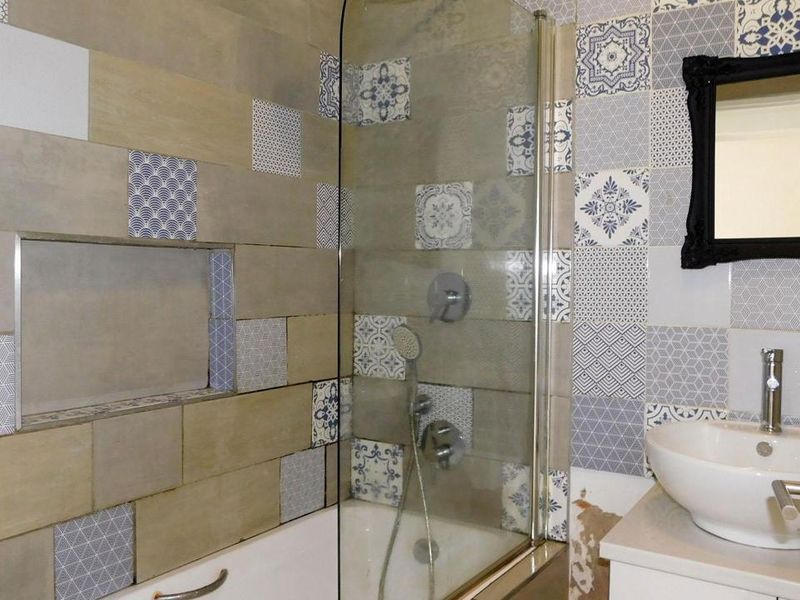 Bathroom featuring a bathtub with shower screen, recessed wall niche, and vanity basin with decorative patterned wall tiles.