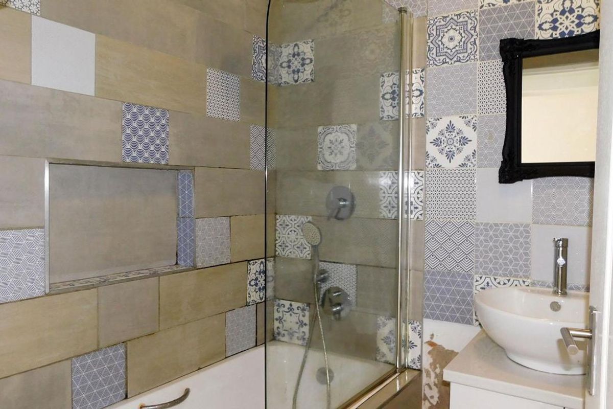 Bathroom featuring a bathtub with shower screen, recessed wall niche, and vanity basin with decorative patterned wall tiles.