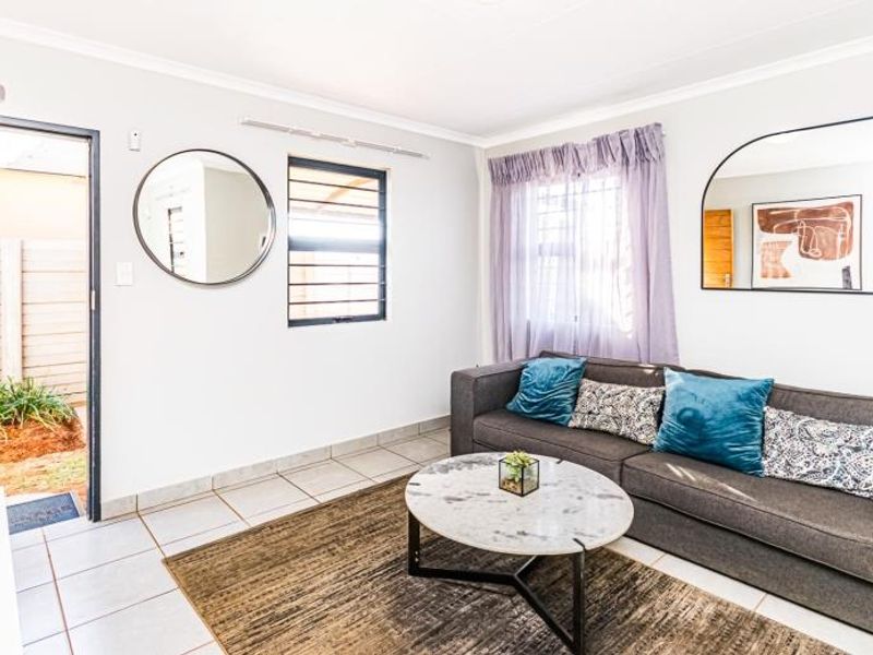 A bright living room featuring tiled flooring, security bars on windows, and direct access to an outdoor area.