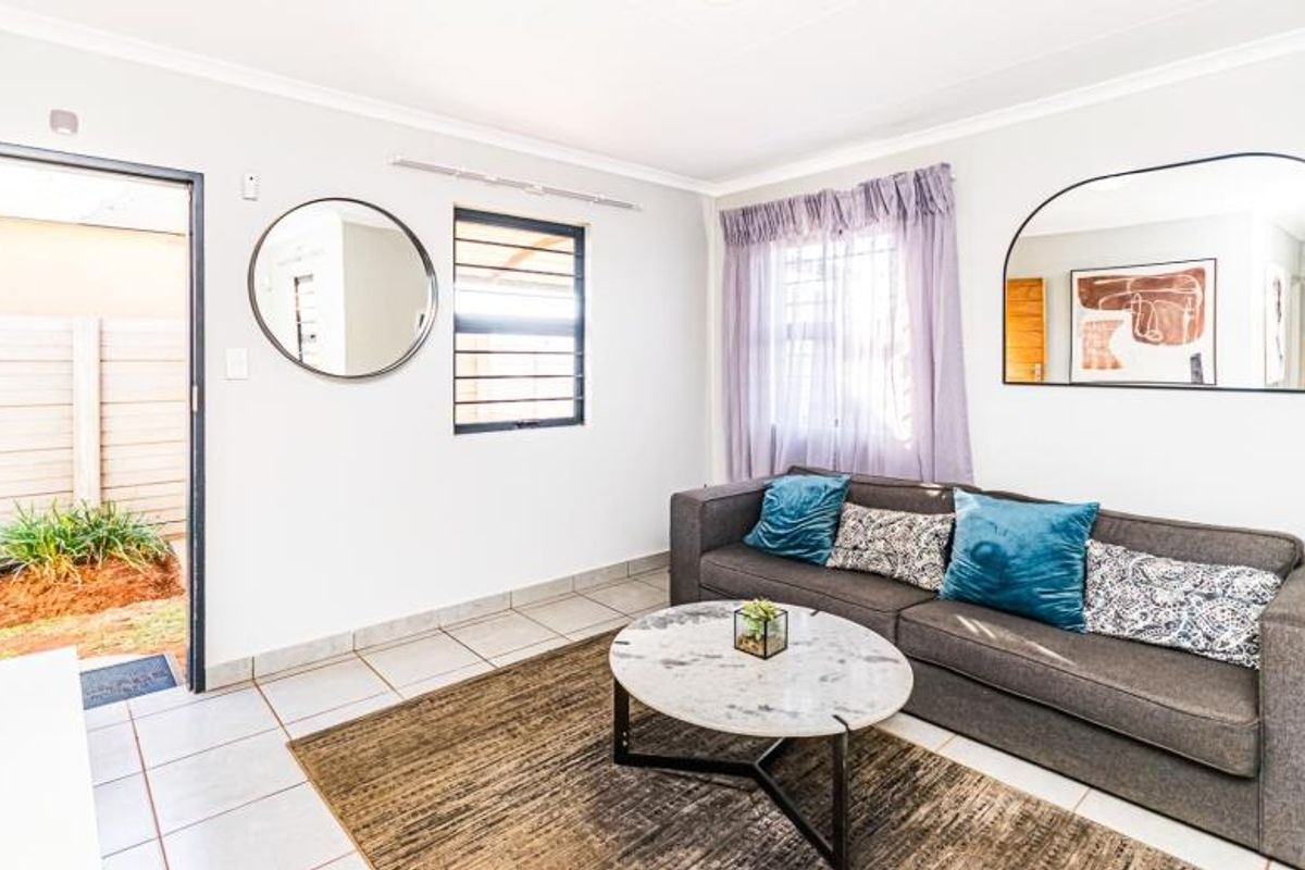 A bright living room featuring tiled flooring, security bars on windows, and direct access to an outdoor area.