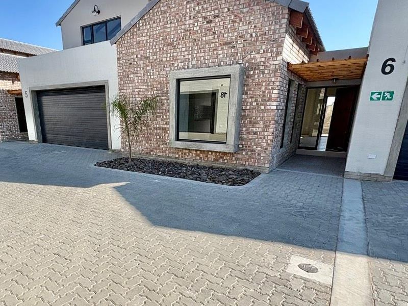 Modern townhouse exterior featuring a brick facade, paved driveway, integrated garage, and a timber pergola over the entrance.