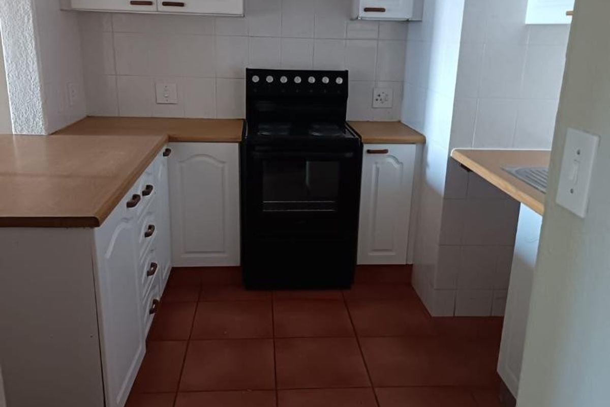 A functional kitchen featuring white cabinetry, wooden countertops, a freestanding stove, and tiled flooring with a neutral tiled backsplash.