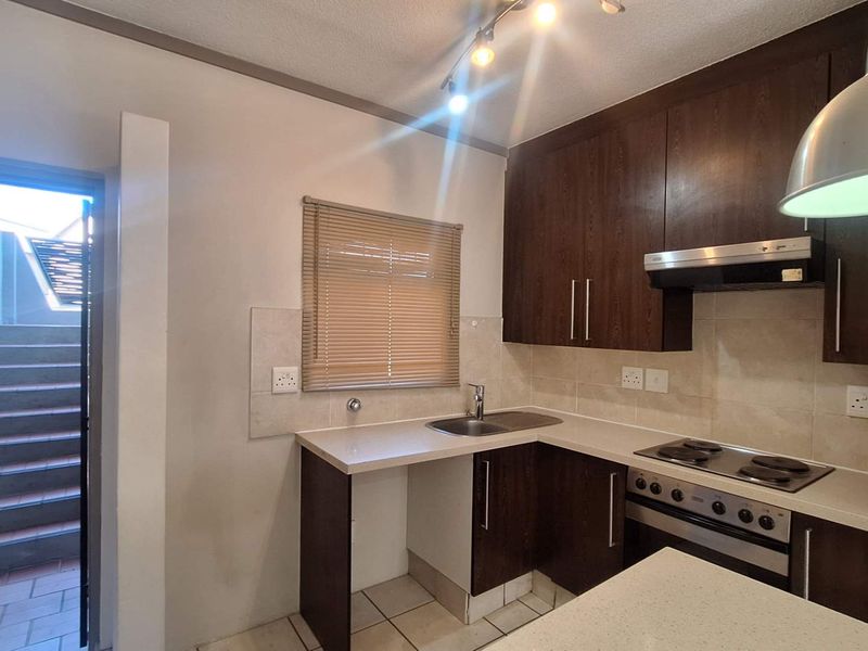 Compact kitchen featuring dark wood cabinetry, built-in oven with extractor fan, and tiled backsplash, with direct access to an external staircase.