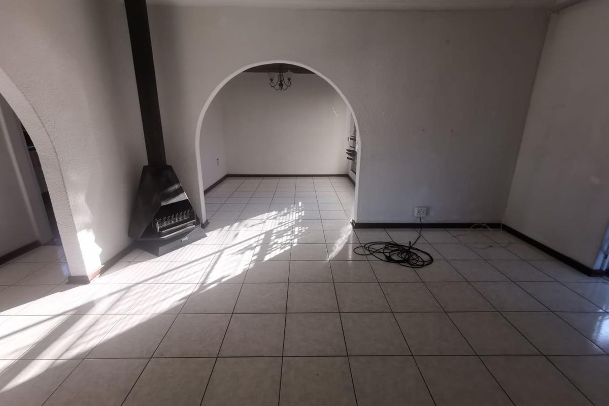 An empty living area featuring tiled flooring, a freestanding fireplace, and distinctive arched doorways leading to adjacent spaces.