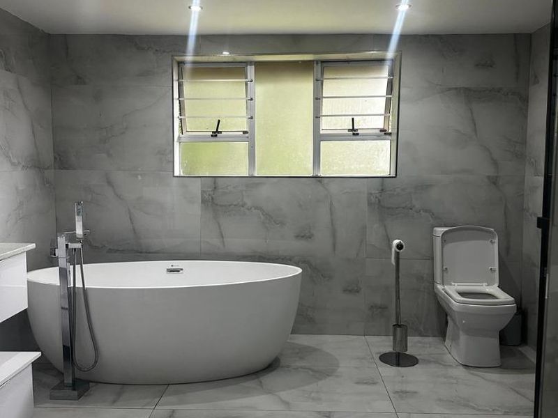 Modern bathroom featuring large format marble-look tiles, a contemporary freestanding bathtub with floor-mounted mixer, and a clean, minimalist aesthetic.