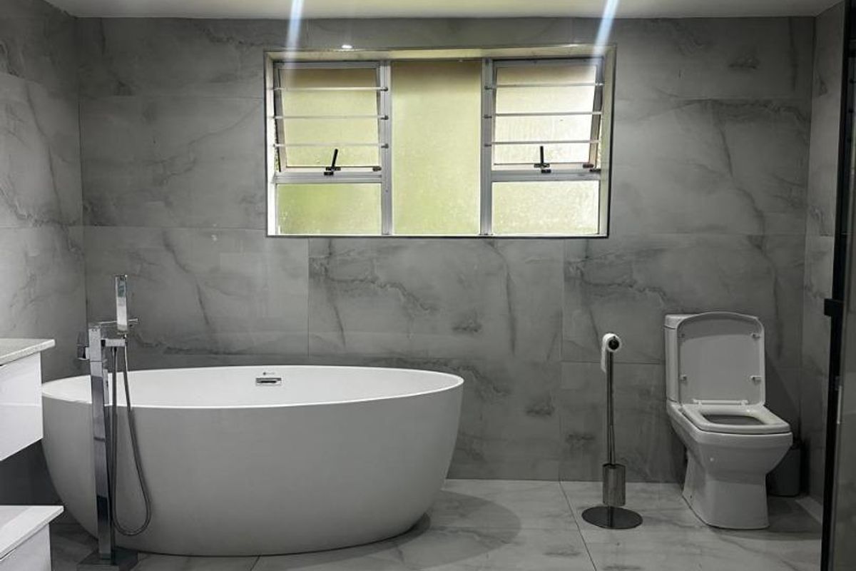 Modern bathroom featuring large format marble-look tiles, a contemporary freestanding bathtub with floor-mounted mixer, and a clean, minimalist aesthetic.