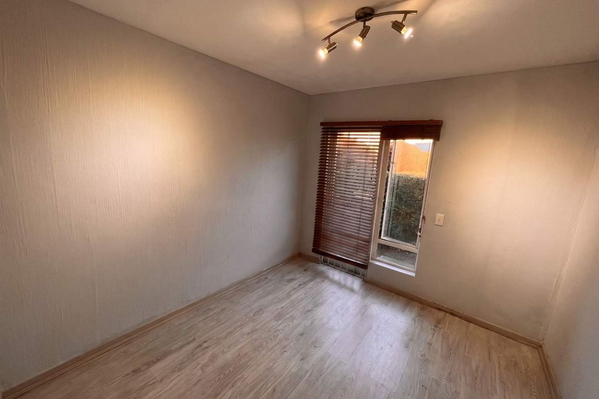 A bright, empty bedroom featuring light-toned laminate flooring, textured walls, and timber venetian blinds, offering a clean and neutral space ready for furnishing.