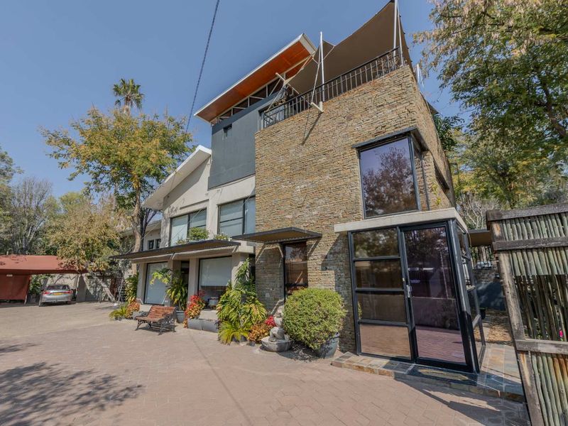 Modern multi-story residence featuring stone cladding, a paved driveway, a private balcony, and a covered carport area.
