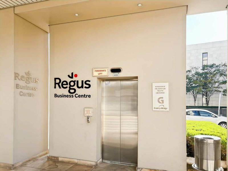 Professional office building entrance featuring a stainless steel elevator, clear signage, and modern stone flooring in a well-maintained commercial lobby area.