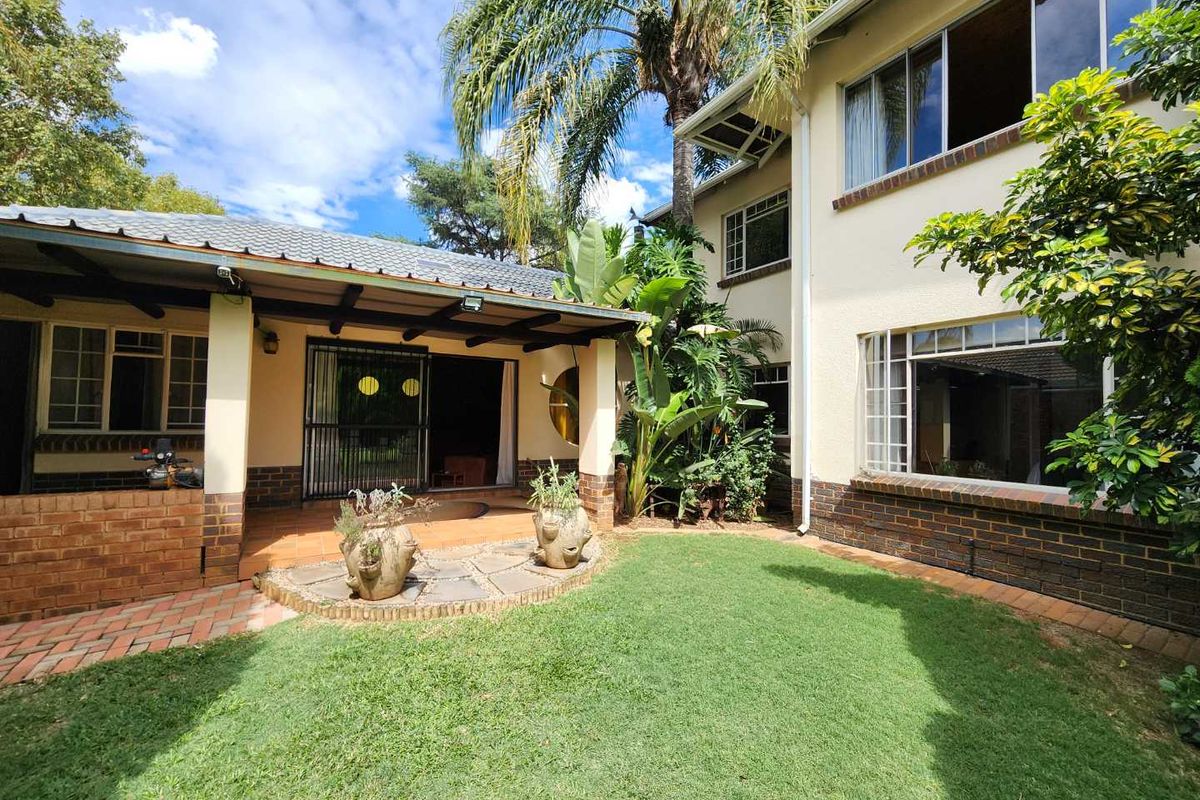 Rear view of the house featuring a covered patio area, brick base detailing, and a well-maintained garden with mature landscaping.