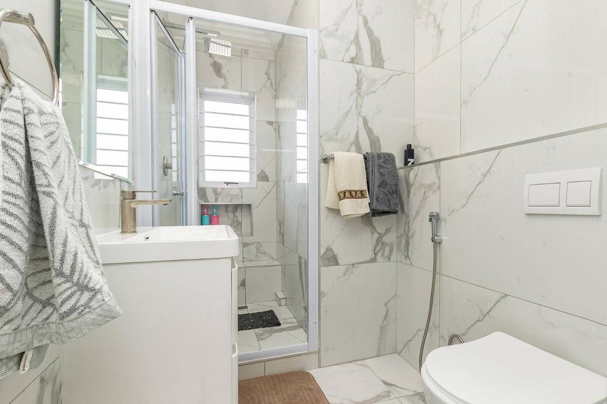Modern bathroom featuring floor-to-ceiling marble-look tiling, a glass-enclosed shower, a wall-mounted toilet, and a contemporary vanity unit.