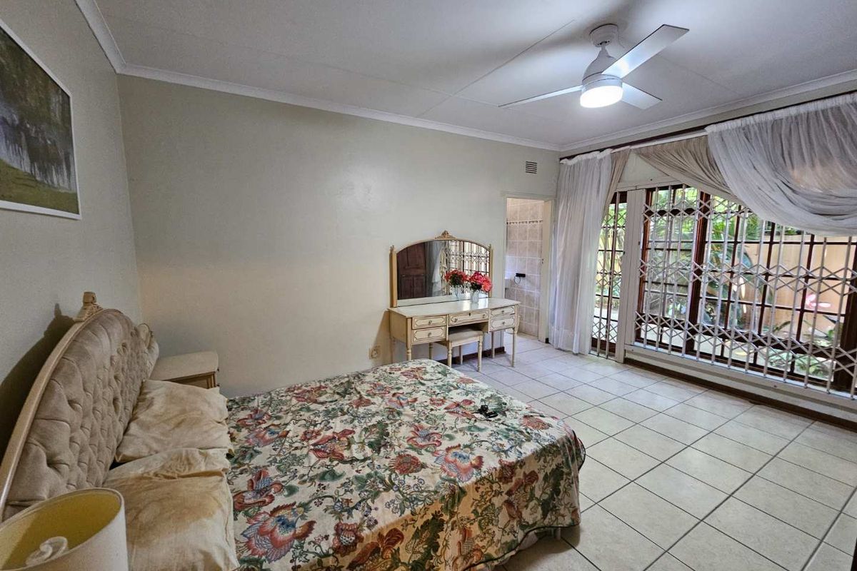 Spacious bedroom featuring tiled flooring, a ceiling fan, and large sliding doors with security gates leading to the exterior.