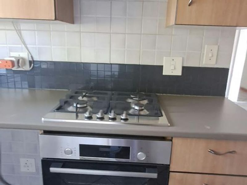 A functional kitchen area featuring a built-in oven, gas hob, extractor fan, and tiled backsplash with laminate cabinetry.
