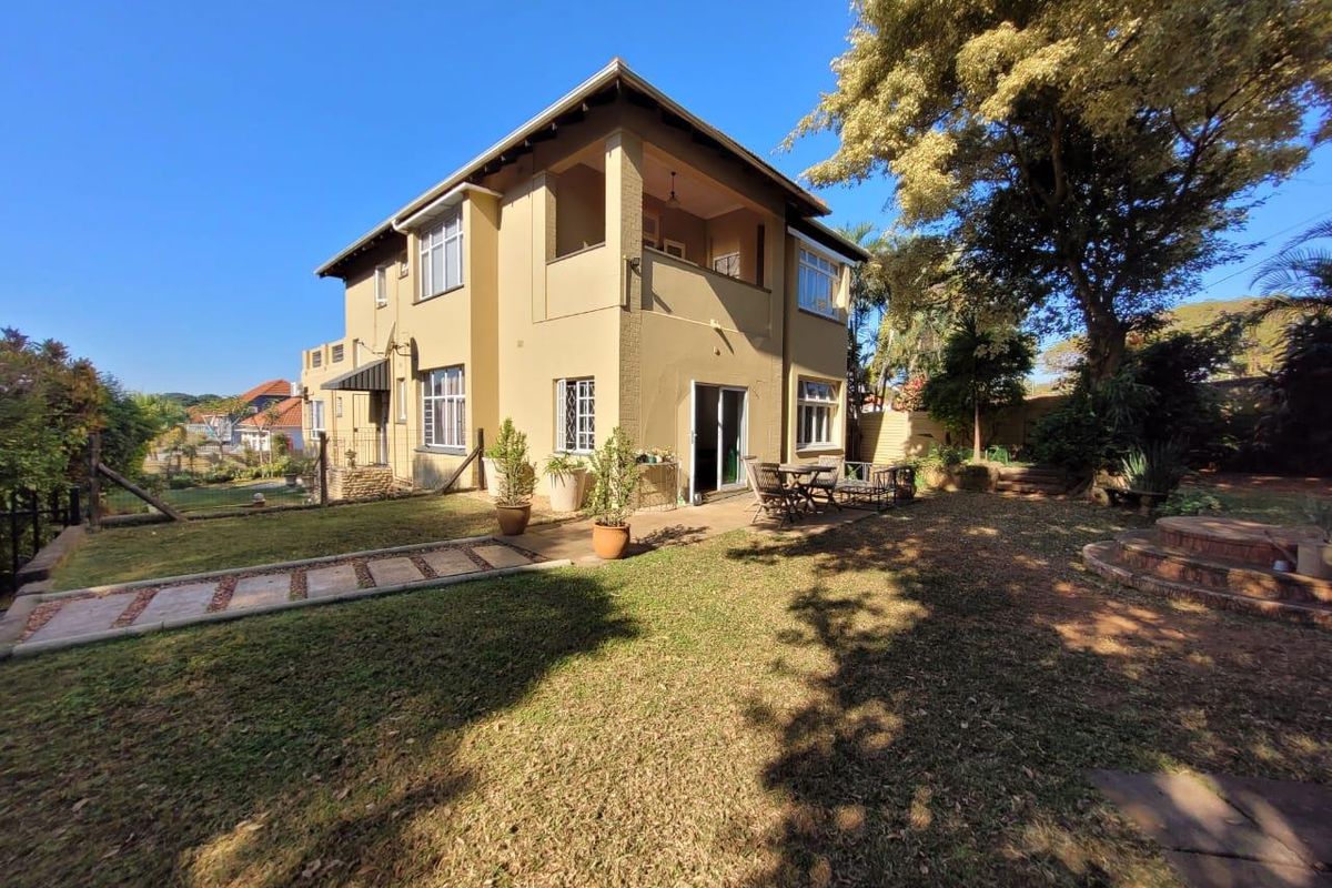Rear view of a two-story house featuring a covered balcony, paved patio area, and a spacious landscaped garden.