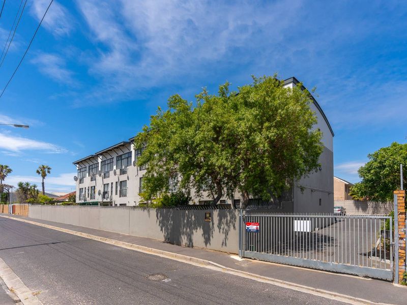 Street view of the apartment complex featuring a secure perimeter wall, sliding gate access, and multi-story building facade.