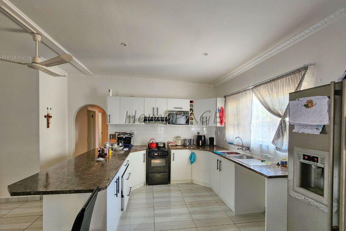 A functional kitchen featuring white cabinetry, granite countertops, a built-in oven with extractor fan, and tiled flooring with an open-plan layout.