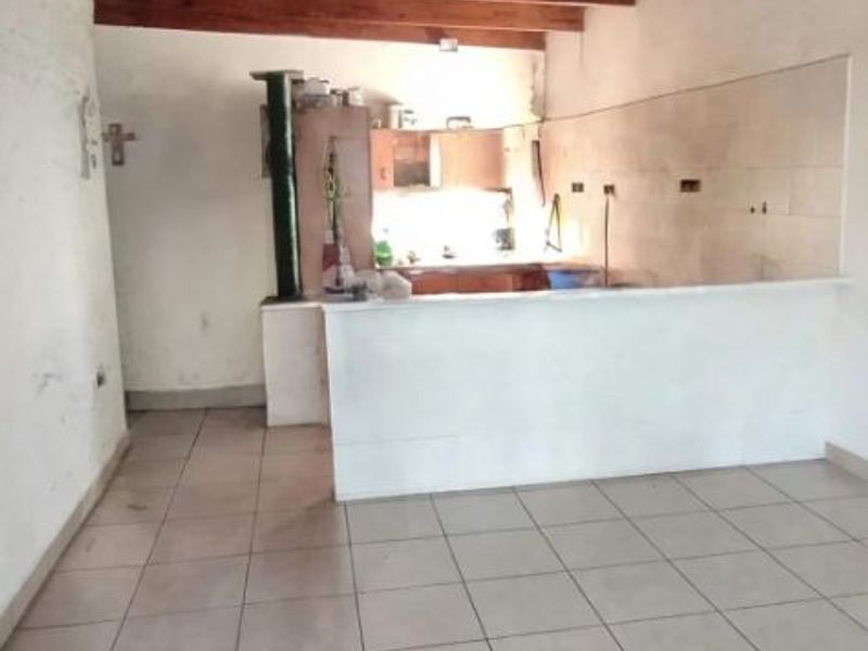 Open plan living and kitchen area featuring exposed timber beam ceilings, tiled flooring, and a central breakfast bar with a built-in fireplace.