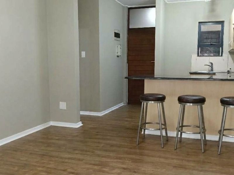Open plan living and kitchen area featuring laminate flooring, neutral walls, and a functional kitchen with granite countertops and built-in cabinetry.