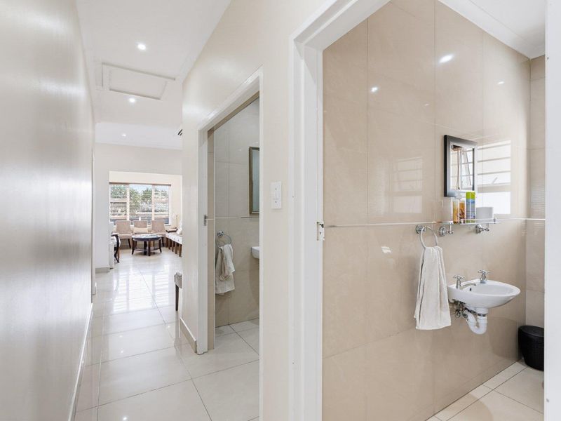 A bright, tiled hallway providing access to a bathroom and an open-plan living area, featuring modern finishes and recessed lighting.