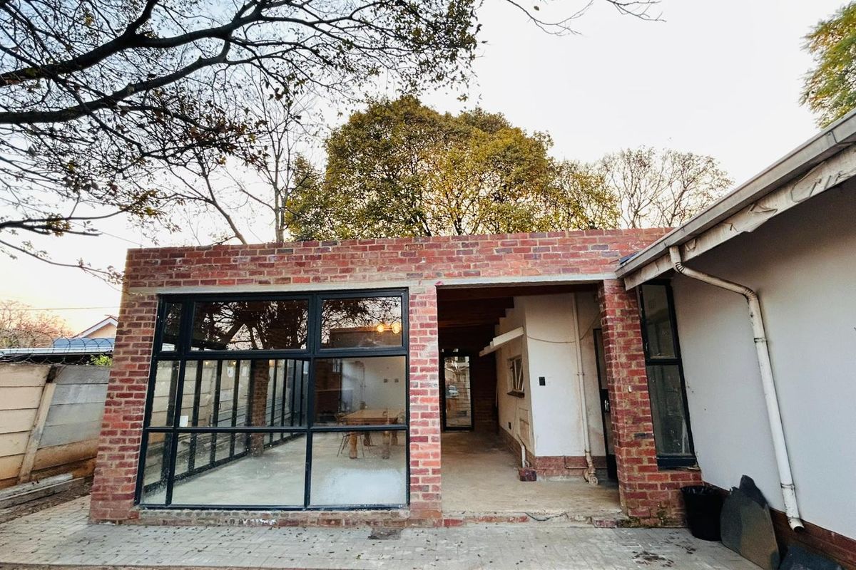 Rear view of a house extension featuring exposed brickwork, large black-framed glass windows, and an open-plan transition area leading into the interior.