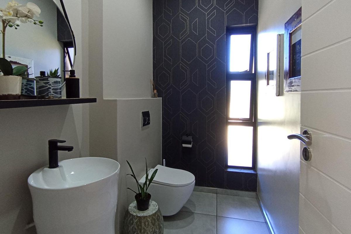 A modern guest bathroom featuring a wall-mounted toilet, a sleek pedestal basin with a black faucet, and decorative geometric wallpaper.