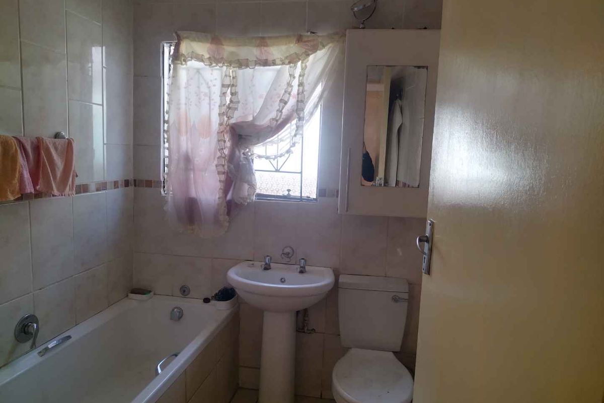A compact bathroom featuring a standard bathtub, pedestal basin, and toilet, finished with wall tiling and a built-in medicine cabinet.